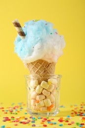 Sweet cotton candy in waffle cone on yellow background, closeup