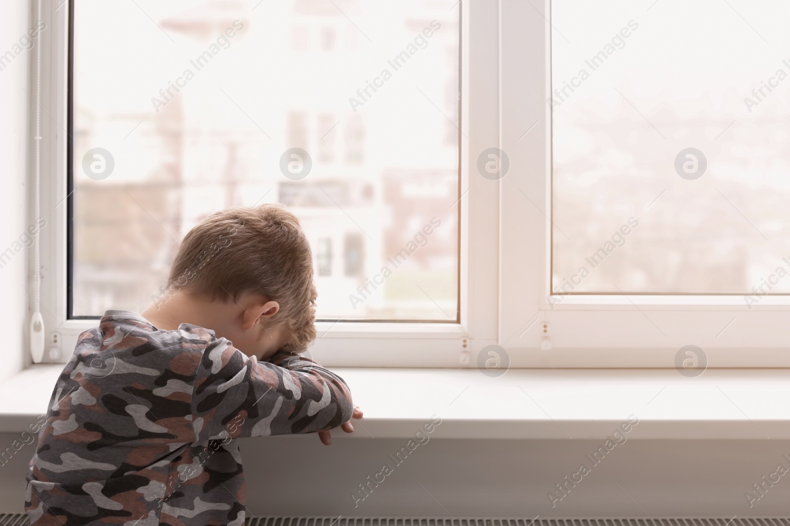 Photo of Lonely little boy near window indoors. Child autism