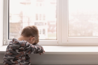 Photo of Lonely little boy near window indoors. Child autism