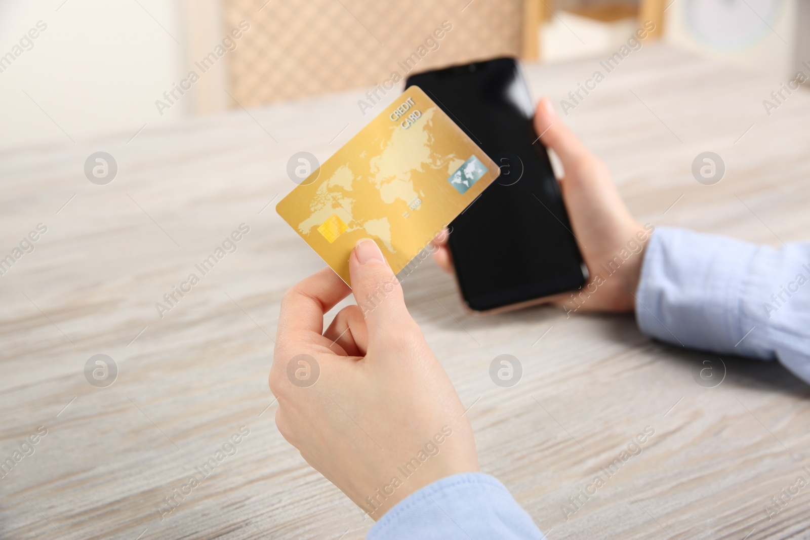 Photo of Online payment. Woman using credit card and smartphone at light wooden table indoors, closeup