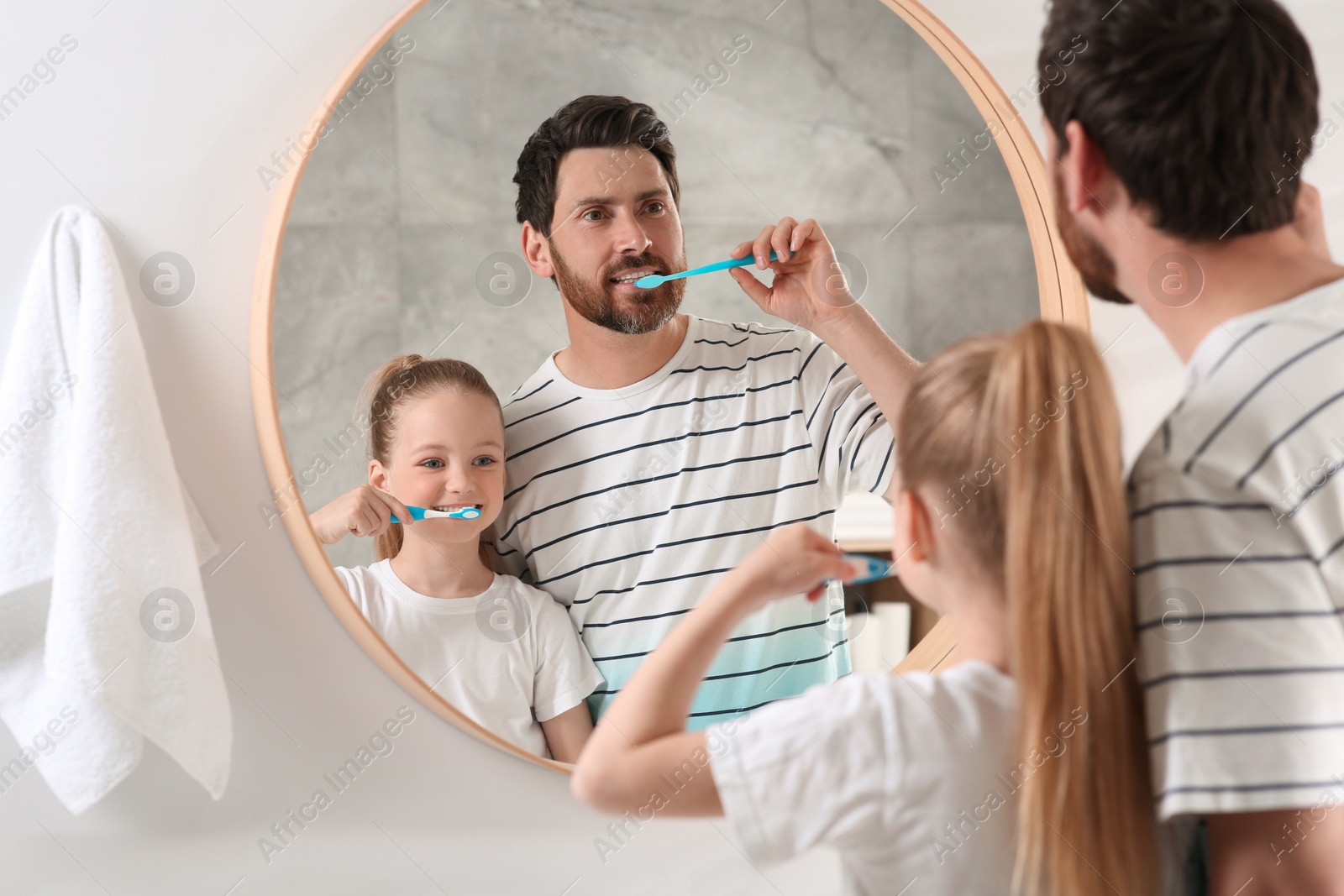 Photo of Father and his daughter brushing teeth together near mirror in bathroom