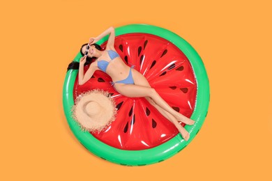 Photo of Happy young woman with beautiful suntan, sunglasses and hat on inflatable mattress against orange background, top view
