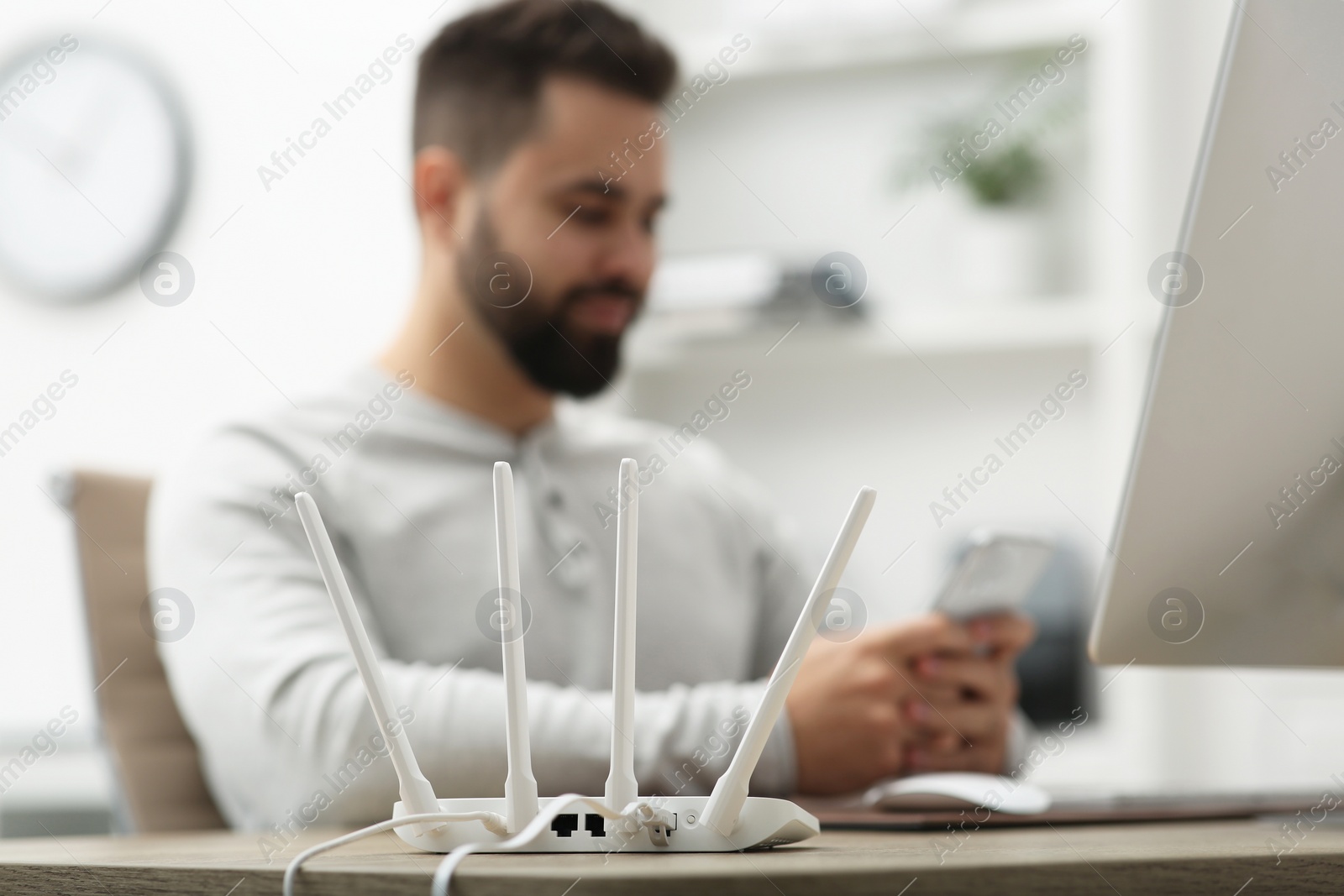 Photo of Man with computer and smartphone working at wooden table, focus on Wi-Fi router
