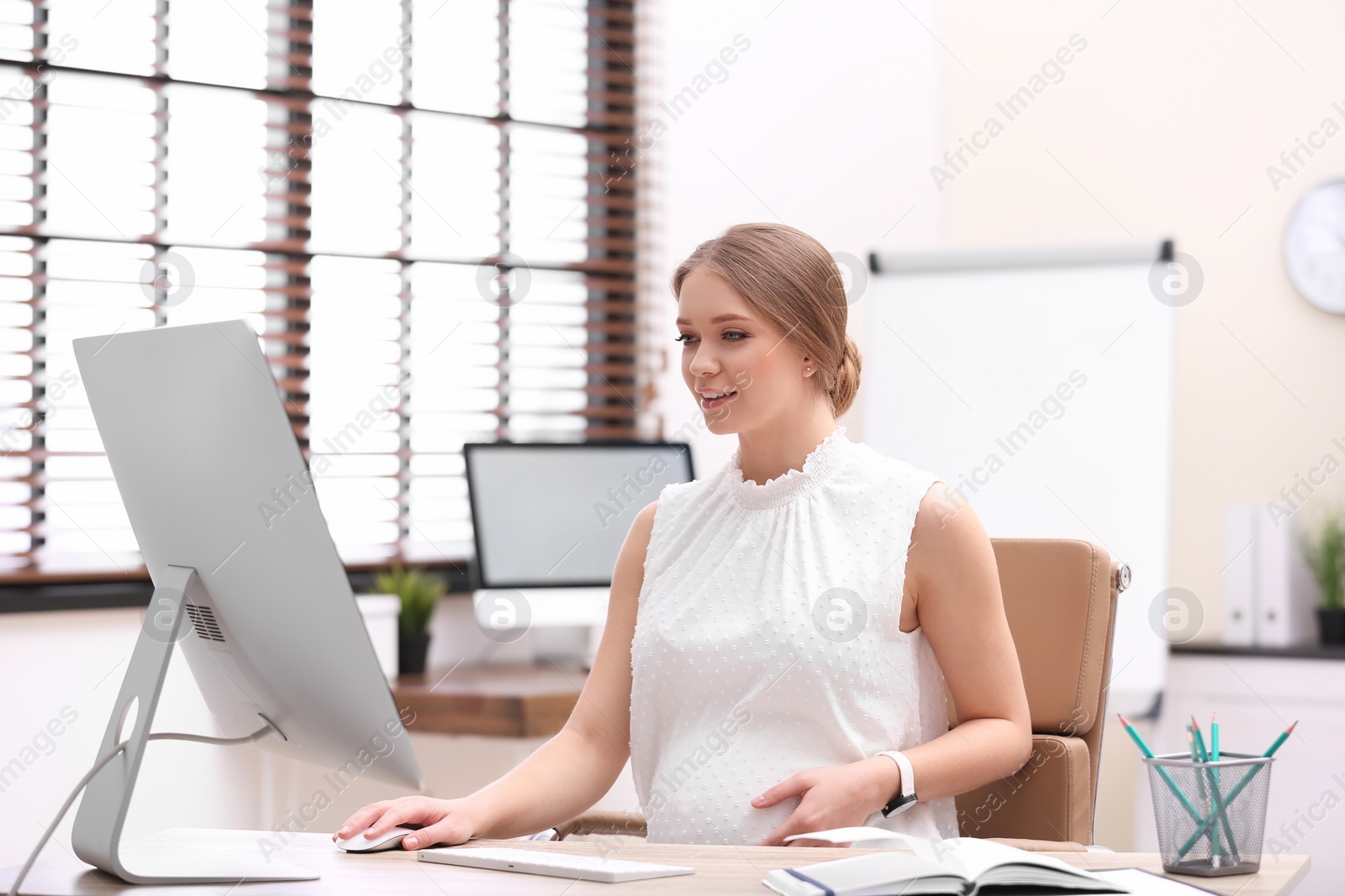 Photo of Young pregnant woman working with computer at table in office