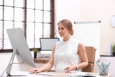 Photo of Young pregnant woman working with computer at table in office