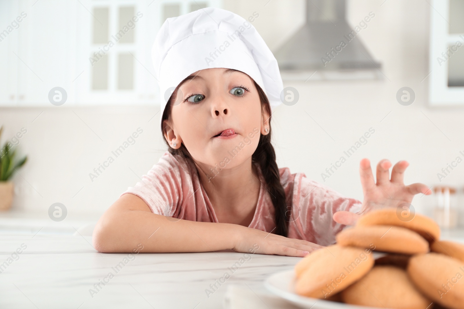 Photo of Cute little girl wearing chef hat at table in kitchen