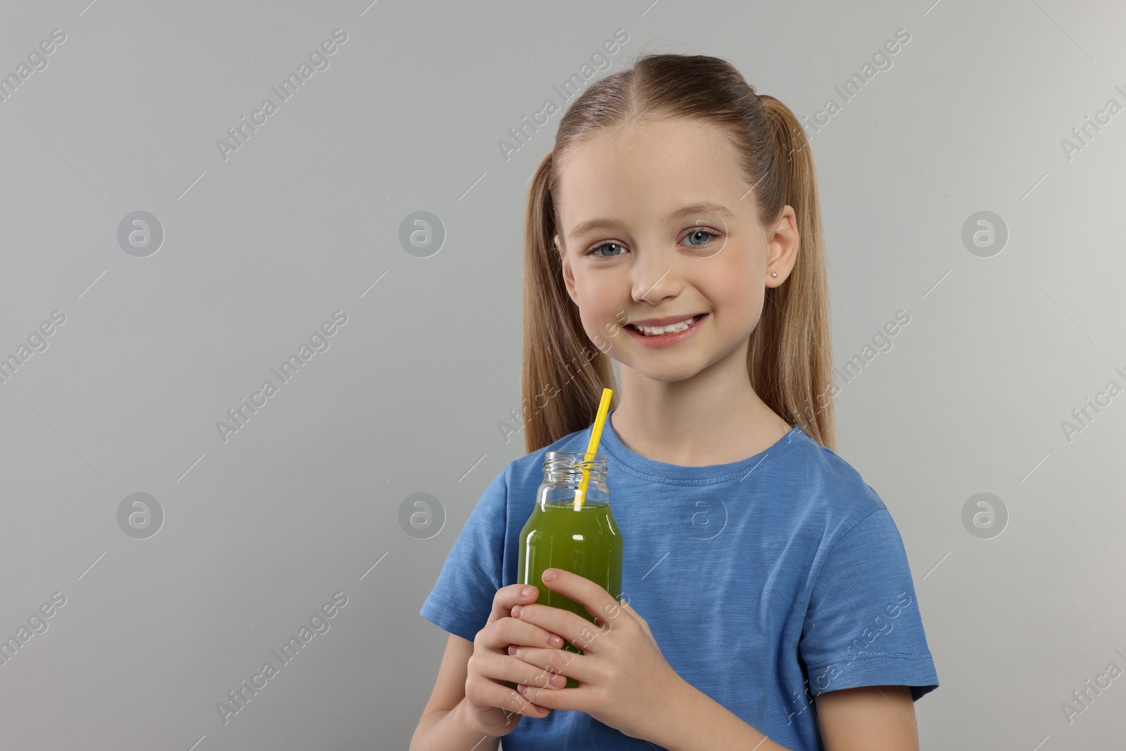 Photo of Cute little girl with glass of fresh juice on light gray background, space for text