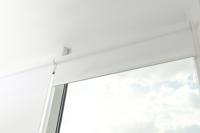 Photo of Modern window with white roller blinds indoors, low angle view