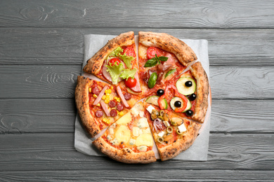 Slices of different delicious pizzas on grey wooden table, top view
