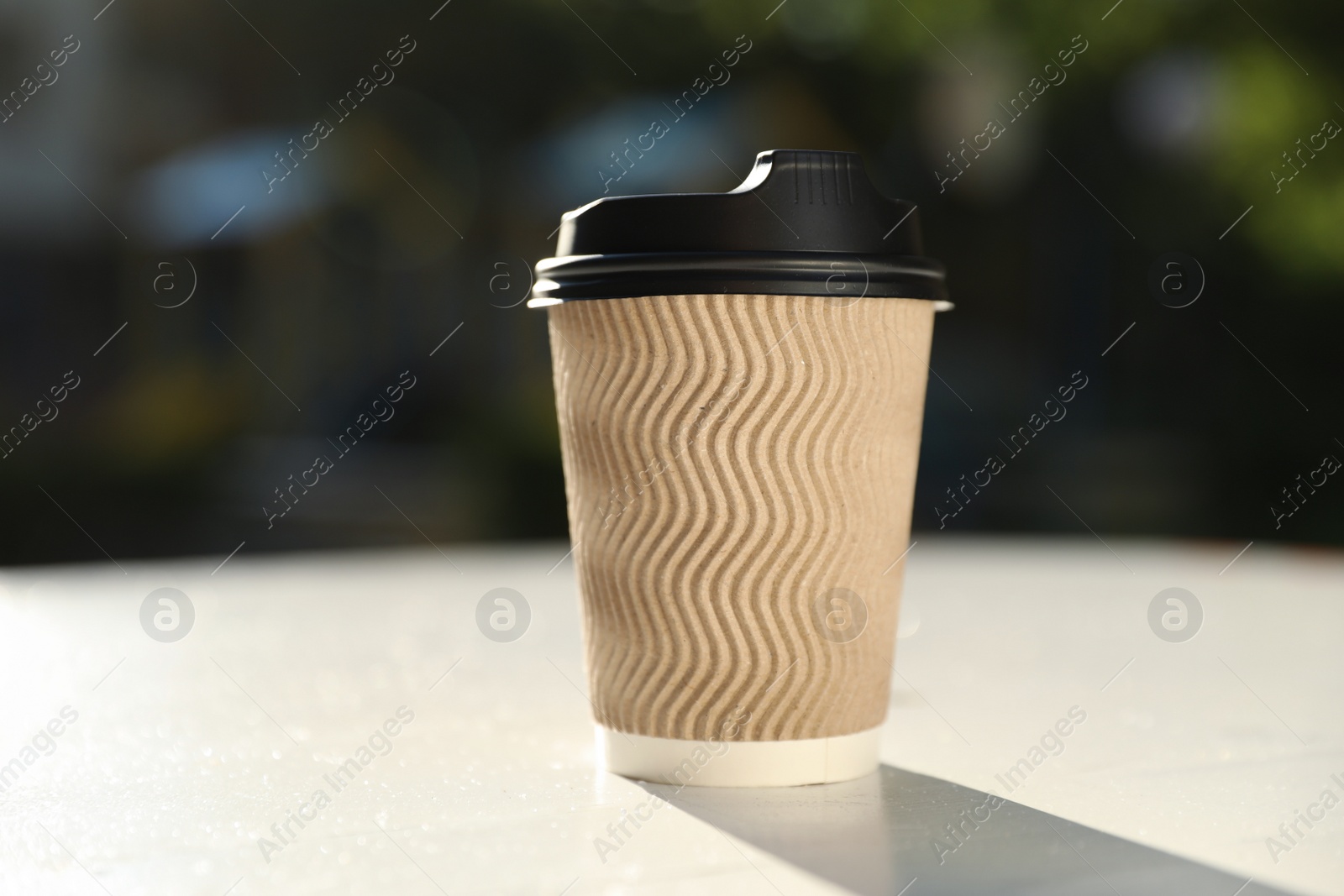 Photo of Cardboard takeaway coffee cup with plastic lid on white table outdoors