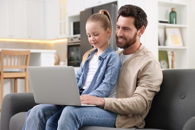 Happy man and his daughter with laptop on sofa at home