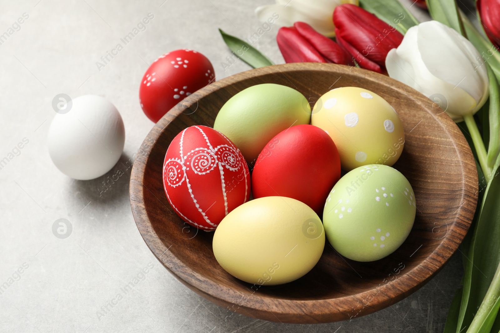 Photo of Bowl with painted Easter eggs and spring flowers on light background