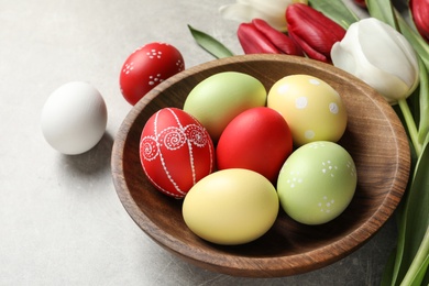 Bowl with painted Easter eggs and spring flowers on light background