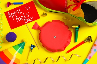 Photo of Sign with phrase April Fools' Day and different clown's accessories on yellow background, flat lay