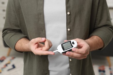 Photo of Diabetes test. Man checking blood sugar level with glucometer at home, closeup