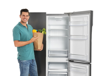 Photo of Man with bag of groceries near open empty refrigerator on white background