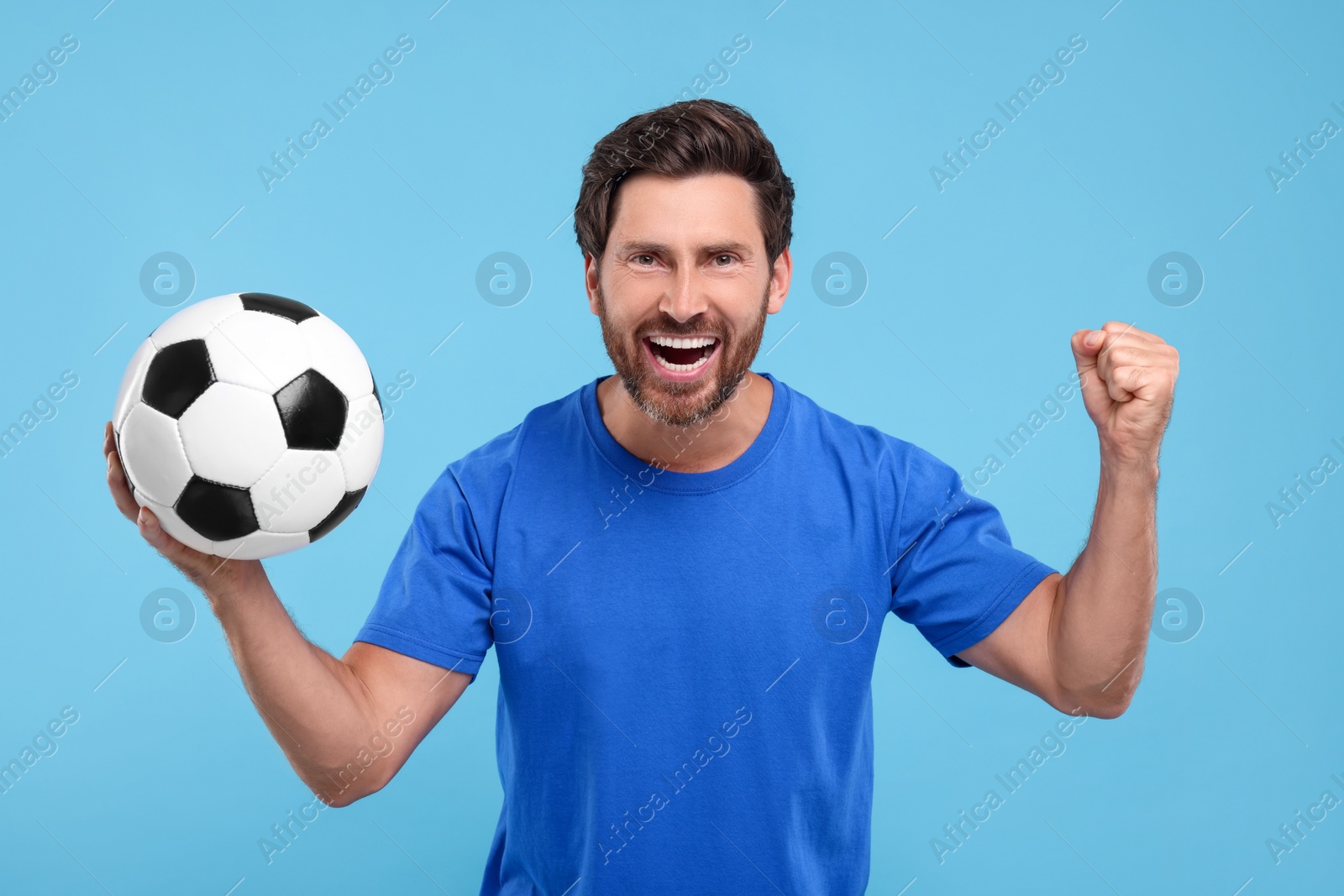 Photo of Emotional sports fan with soccer ball on light blue background