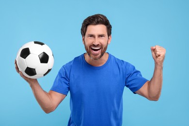 Photo of Emotional sports fan with soccer ball on light blue background