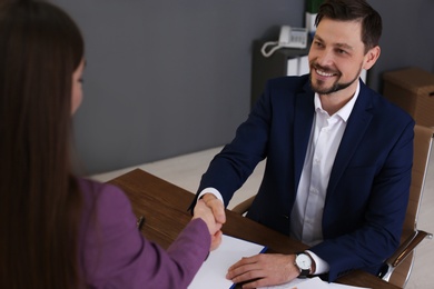 Office employees shaking hands over table with documents at workplace