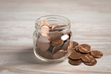 Glass jar with coins on white wooden table, closeup