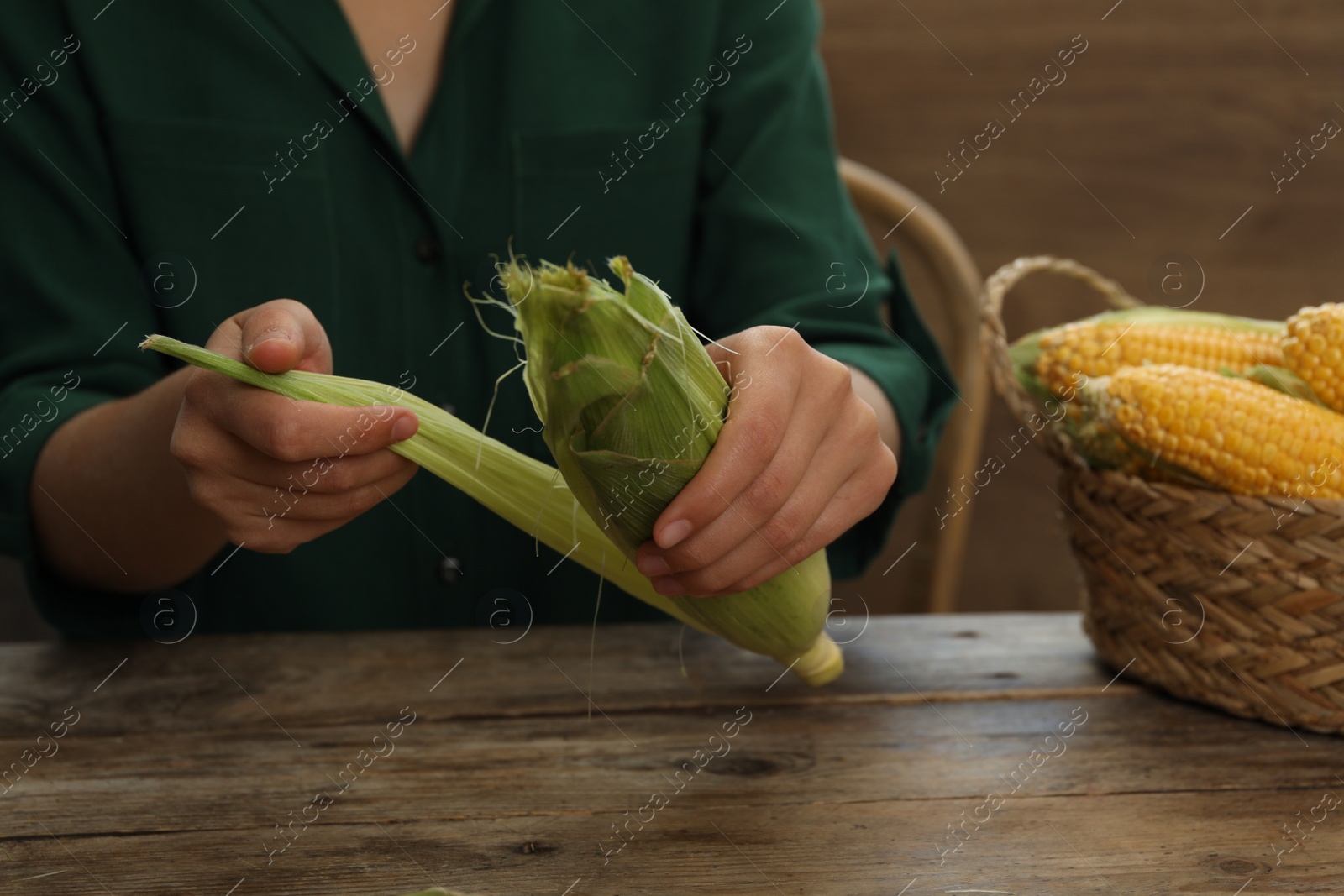 Photo of Woman husking corn cob at wooden table, closeup