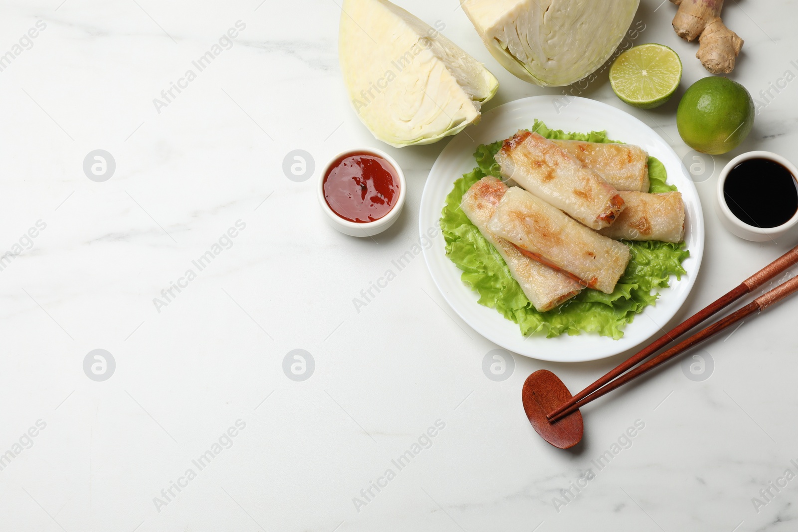 Photo of Delicious fried spring rolls, chopsticks, sauces and ingredients on white marble table, flat lay. Space for text