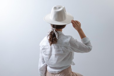 Photo of Young woman with hat and stylish bandana on light background, back view