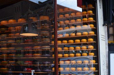 Photo of Amsterdam, Netherlands - June 25, 2022: Many cheese wheels on shelves, view through glass window