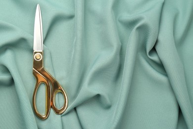 Photo of Scissors on green fabric, top view. Space for text