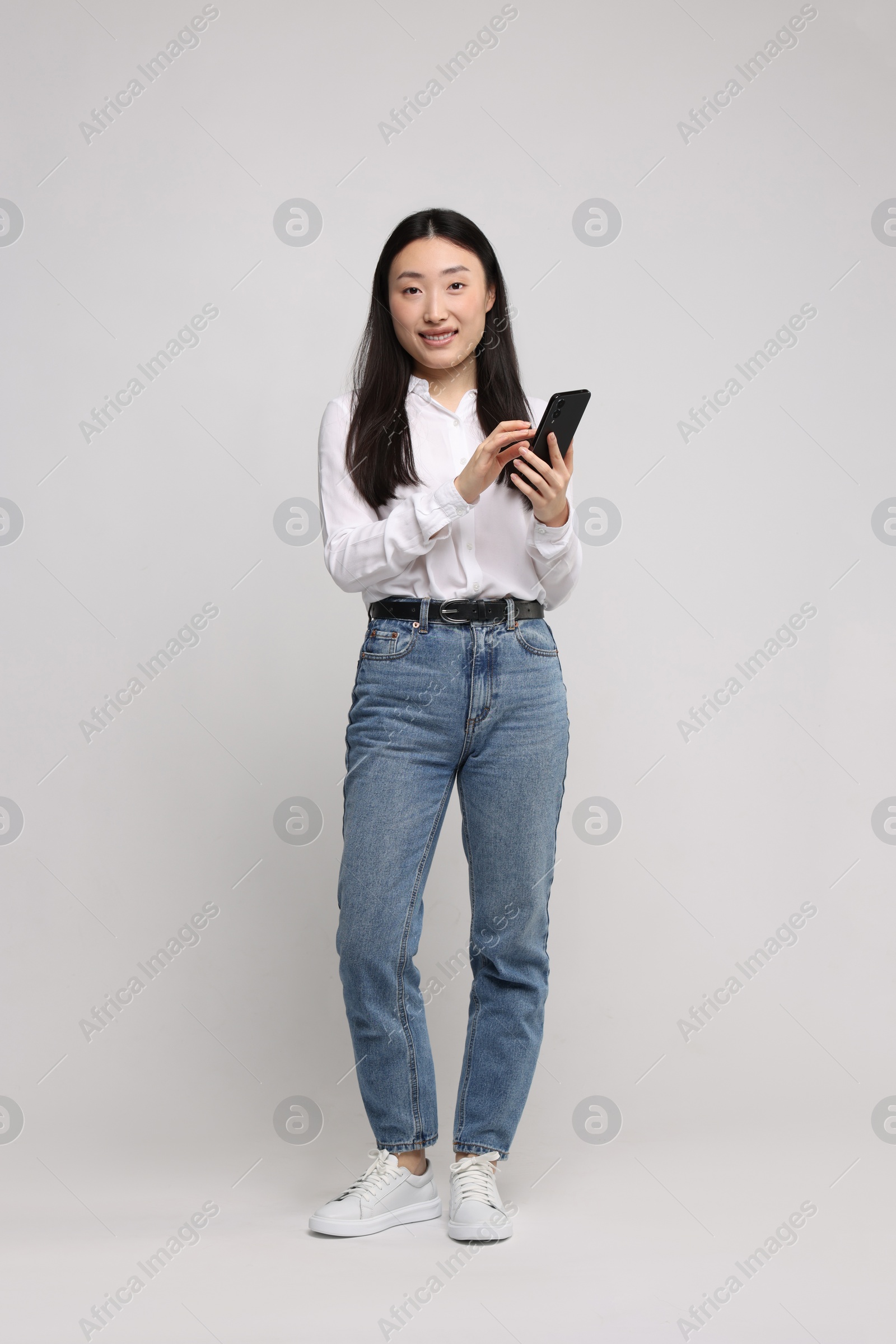 Photo of Full length portrait of smiling woman with smartphone on light background