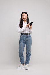 Photo of Full length portrait of smiling woman with smartphone on light background