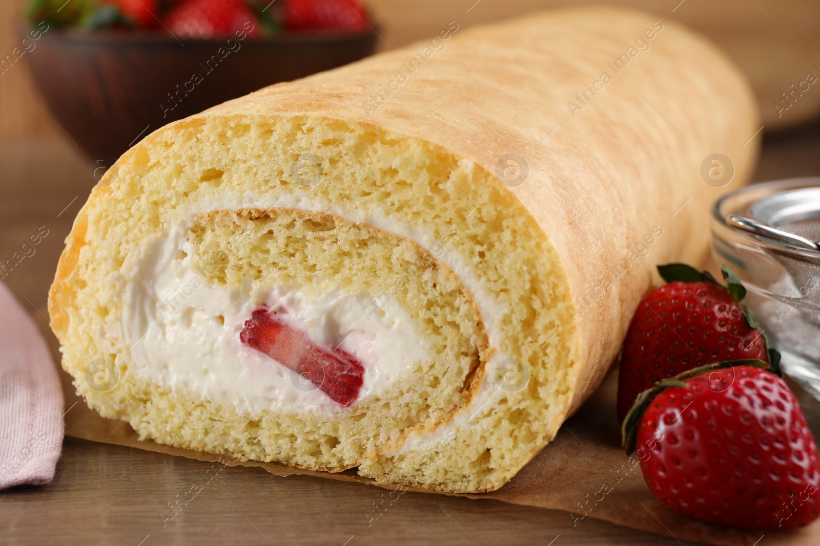 Photo of Delicious sponge cake roll with strawberries and cream on wooden table, closeup