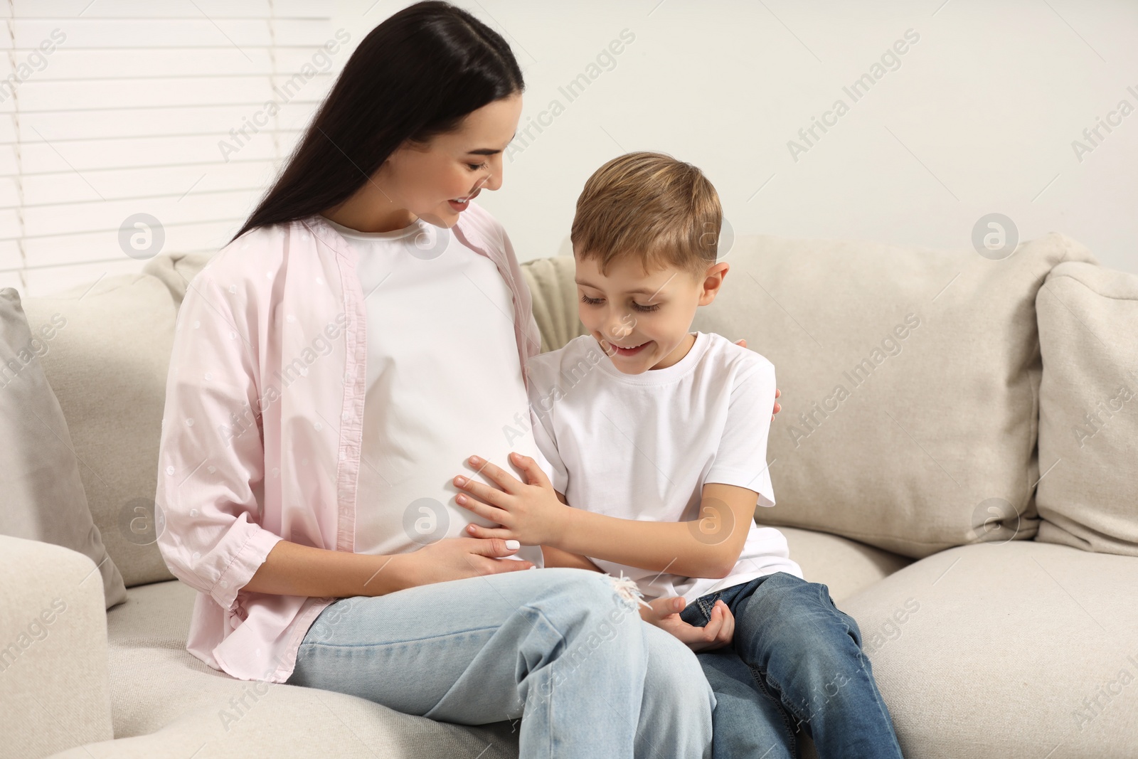 Photo of Cute boy touching pregnant mother's belly at home