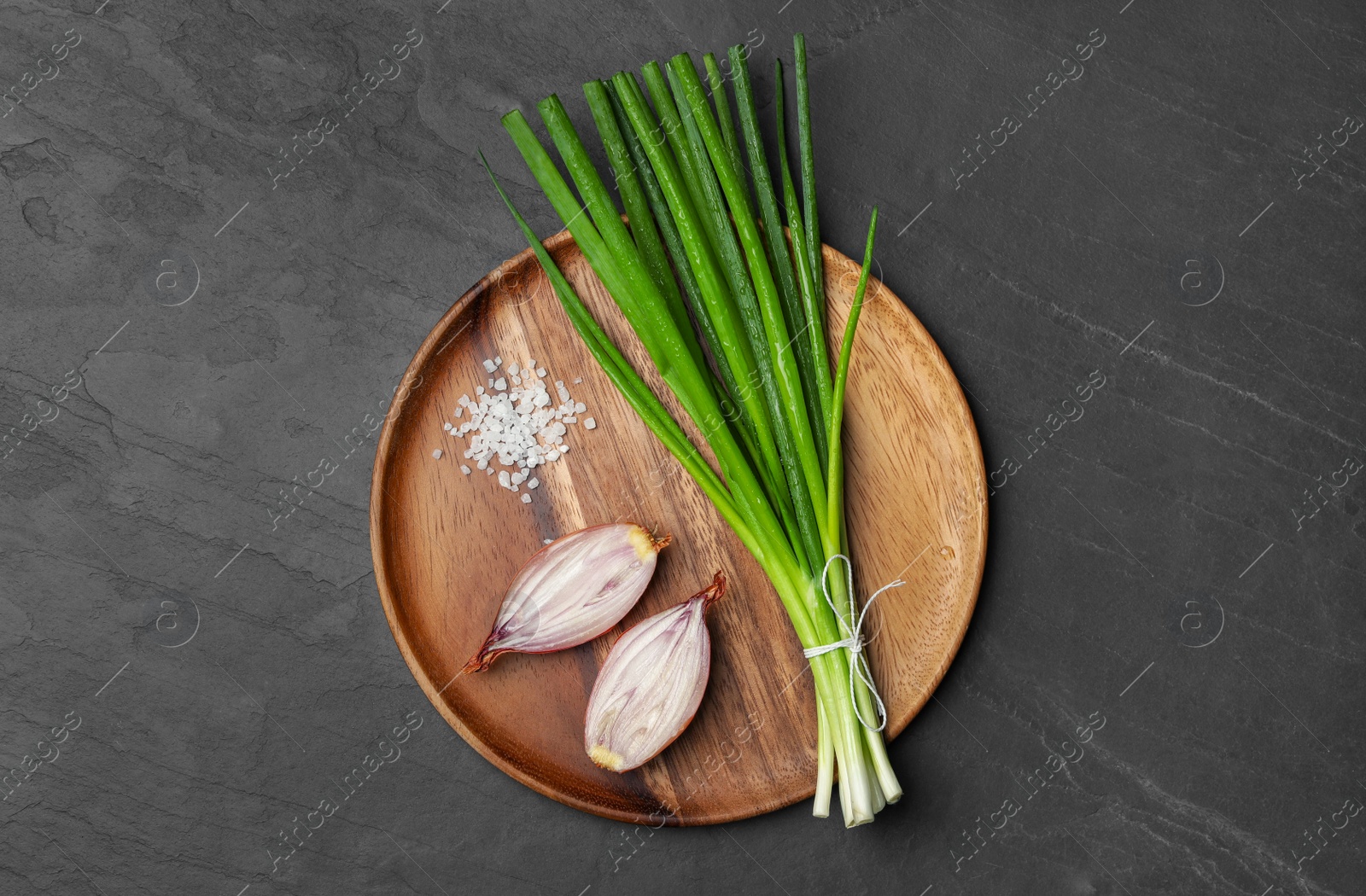 Photo of Bunch of fresh green onion and halved bulb on black table, top view