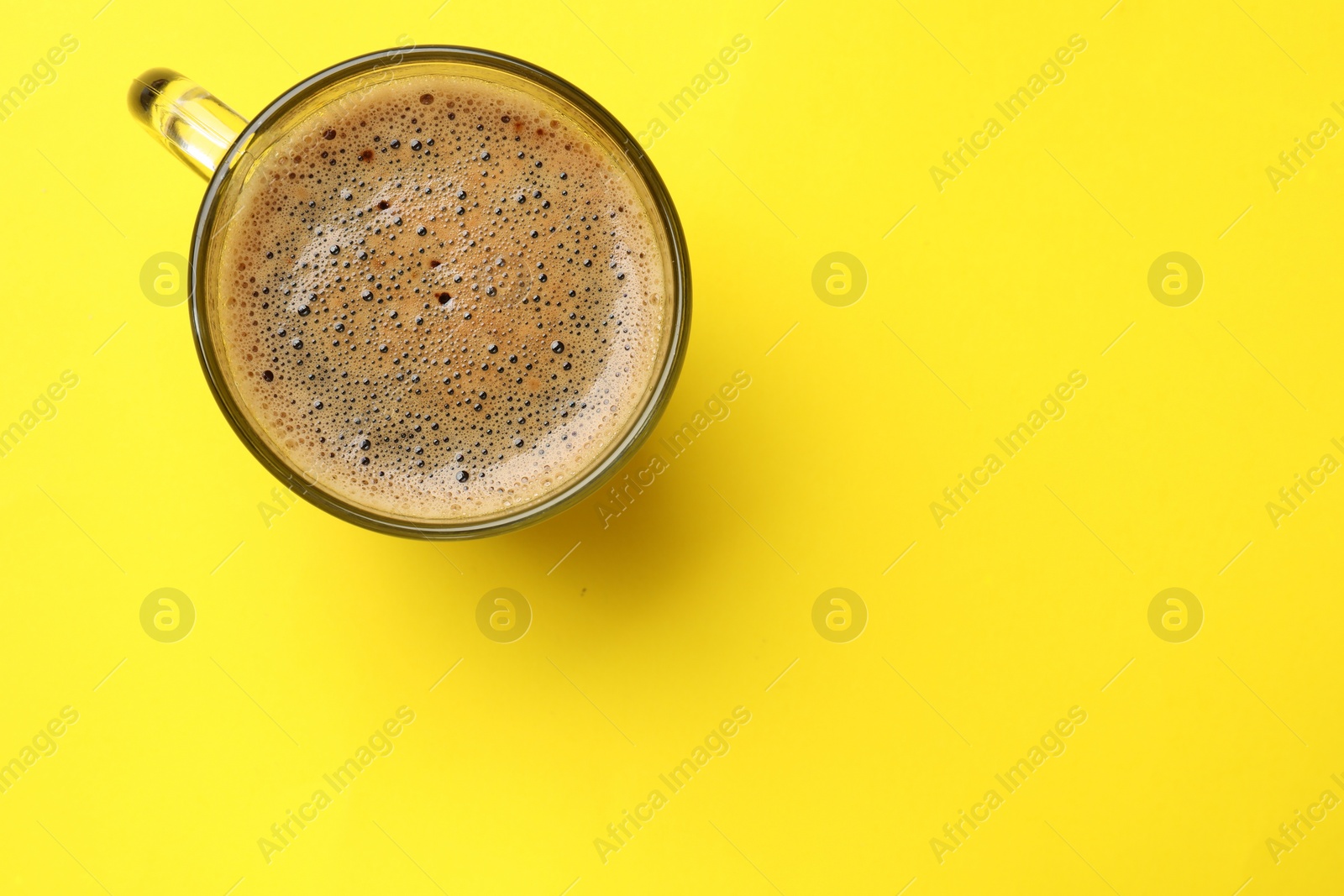 Photo of Aromatic coffee in glass cup on yellow background, top view. Space for text