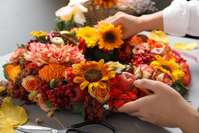 Florist making beautiful autumnal wreath with flowers and fruits at light grey table, closeup