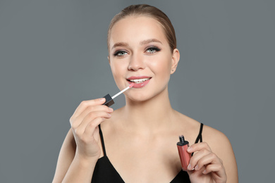 Photo of Beautiful woman applying lip gloss on light grey background. Stylish makeup