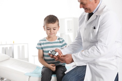 Doctor checking patient's blood sugar level with digital glucometer in hospital. Diabetes control