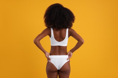 Woman in stylish bikini on yellow background, back view