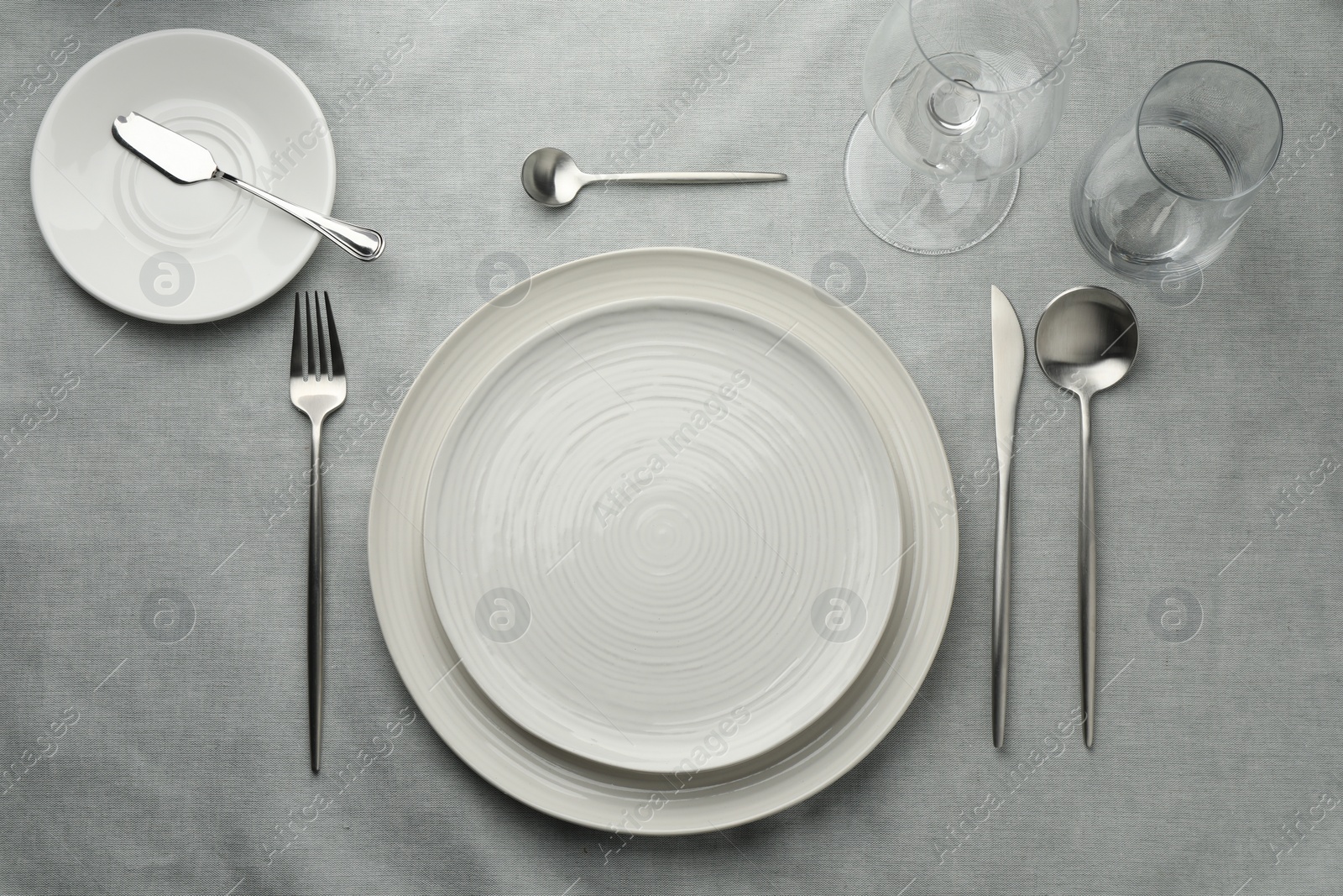 Photo of Stylish setting with cutlery, glasses and plates on grey table, flat lay