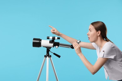 Photo of Surprised astronomer with telescope pointing at something on light blue background, space for text