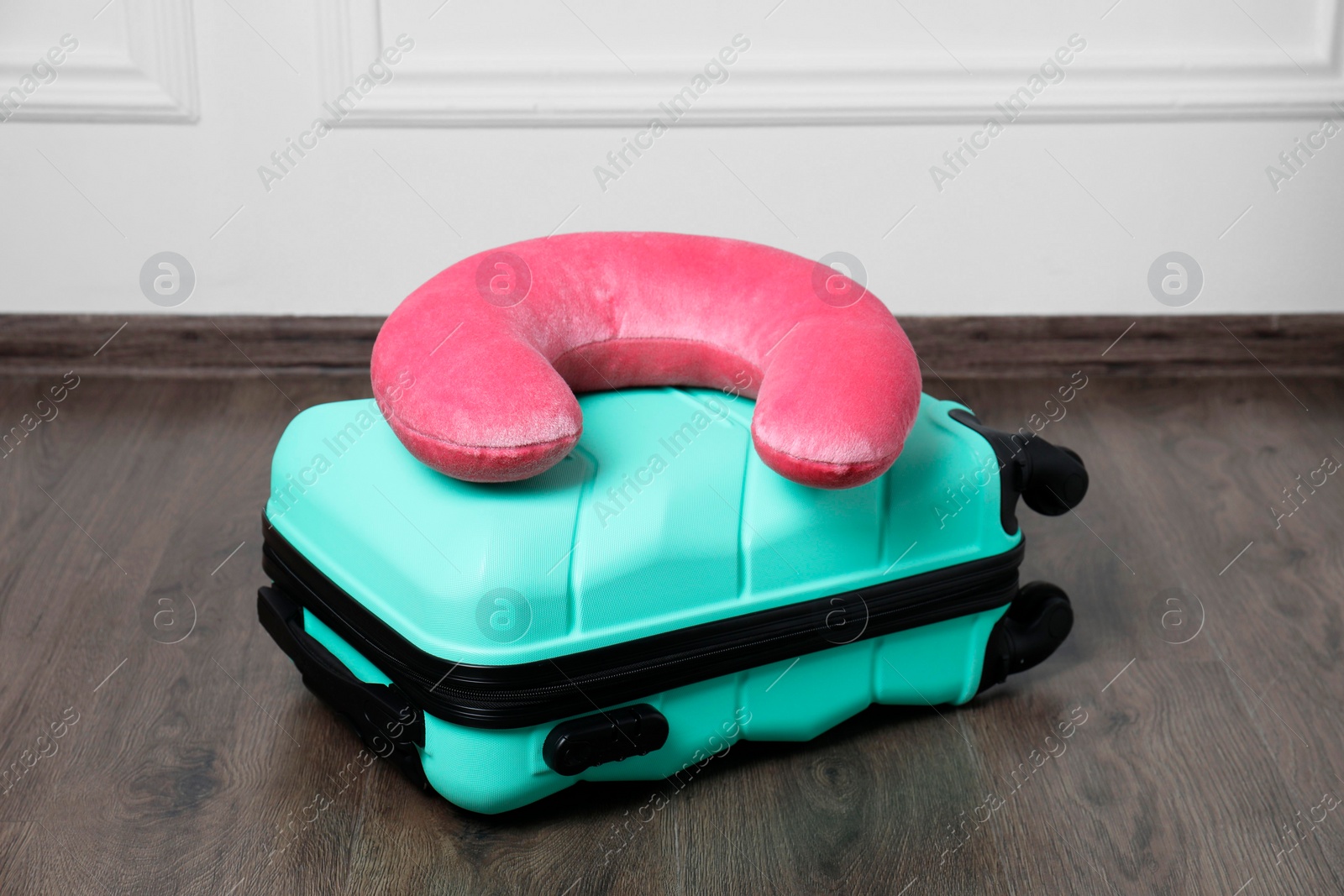 Photo of Pink travel pillow and turquoise suitcase on floor indoors