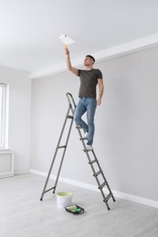 Man painting ceiling with roller on step ladder in room
