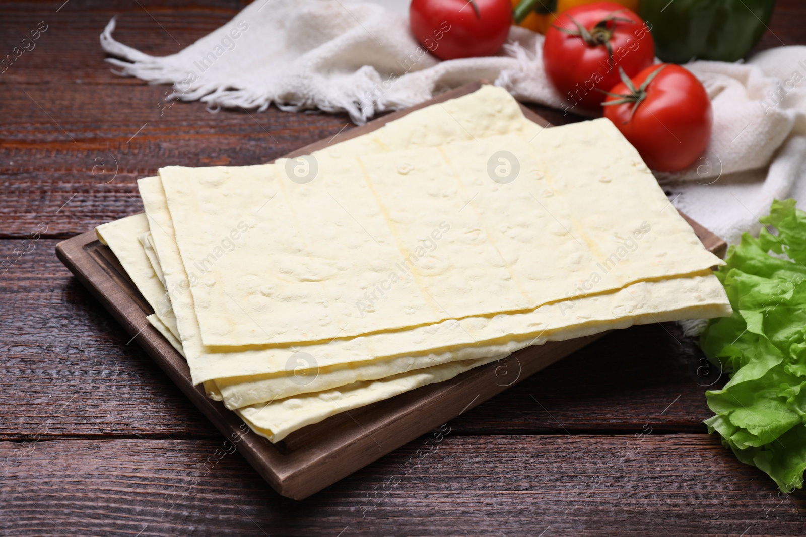 Photo of Delicious folded Armenian lavash and fresh vegetables on wooden table, closeup