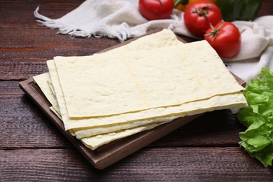 Photo of Delicious folded Armenian lavash and fresh vegetables on wooden table, closeup