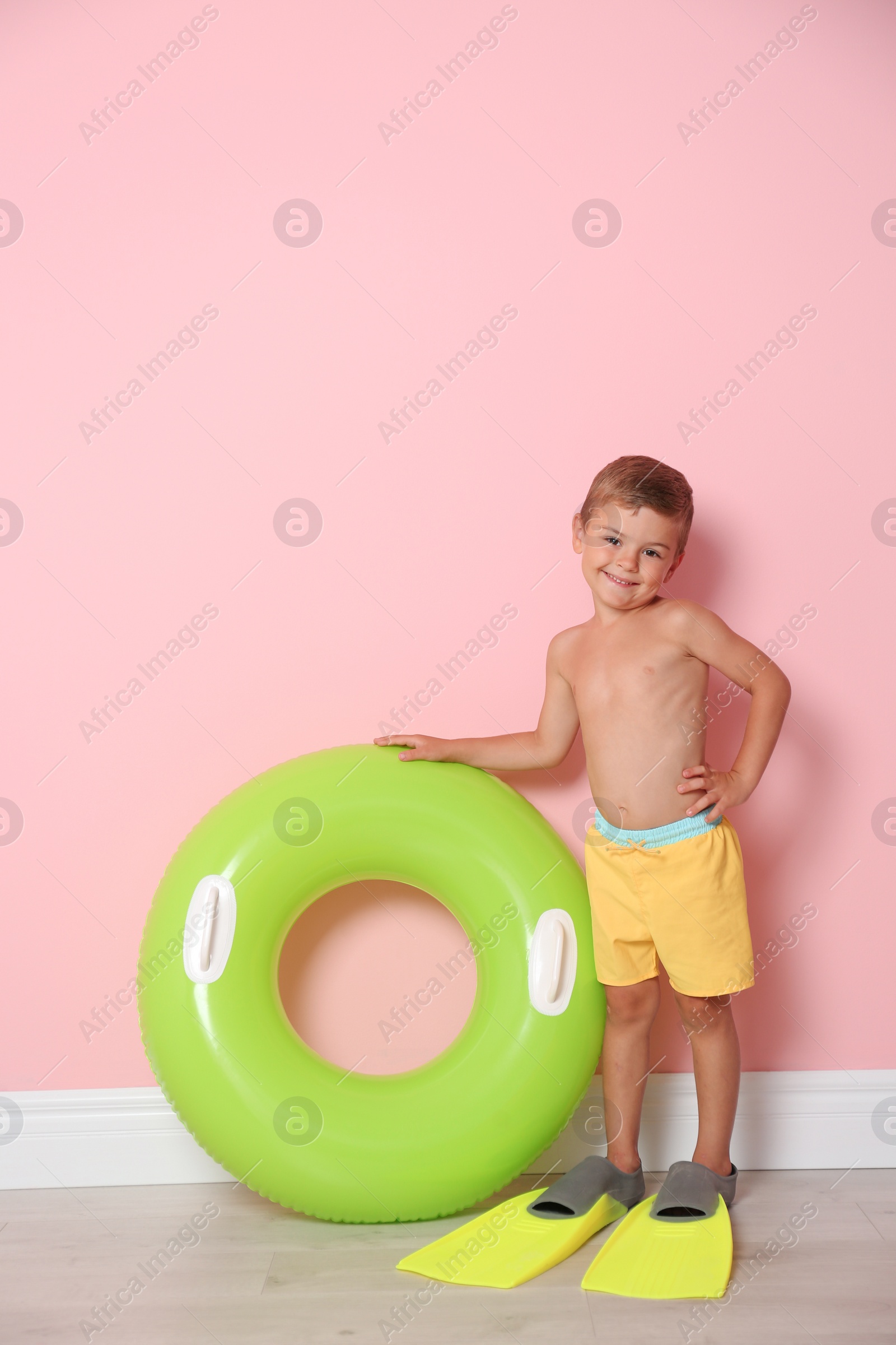 Photo of Cute little boy with inflatable ring wearing flippers near color wall