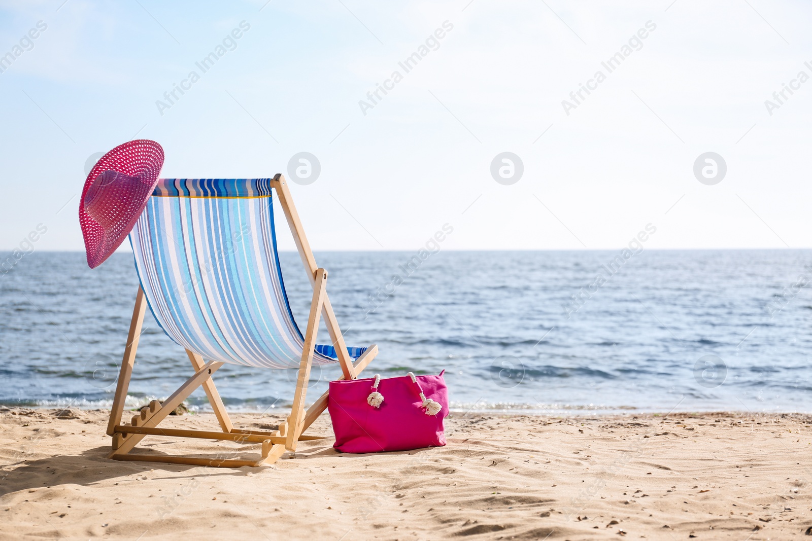 Photo of Lounger, hat and bag on sand near sea, space for text. Beach objects