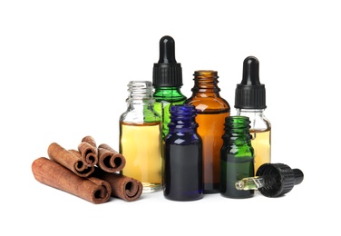 Photo of Bottles of essential oils and cinnamon sticks on white background