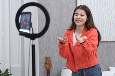 Photo of Smiling teenage blogger explaining something while streaming at home