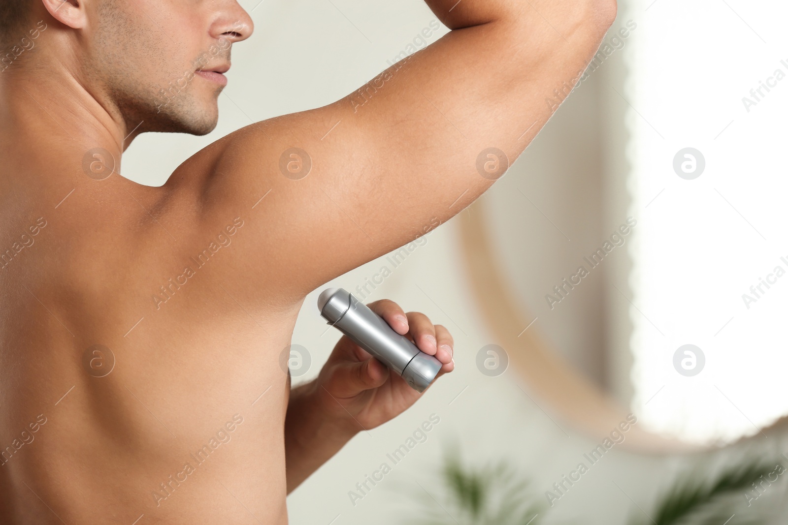 Photo of Young man applying deodorant to armpit indoors, closeup